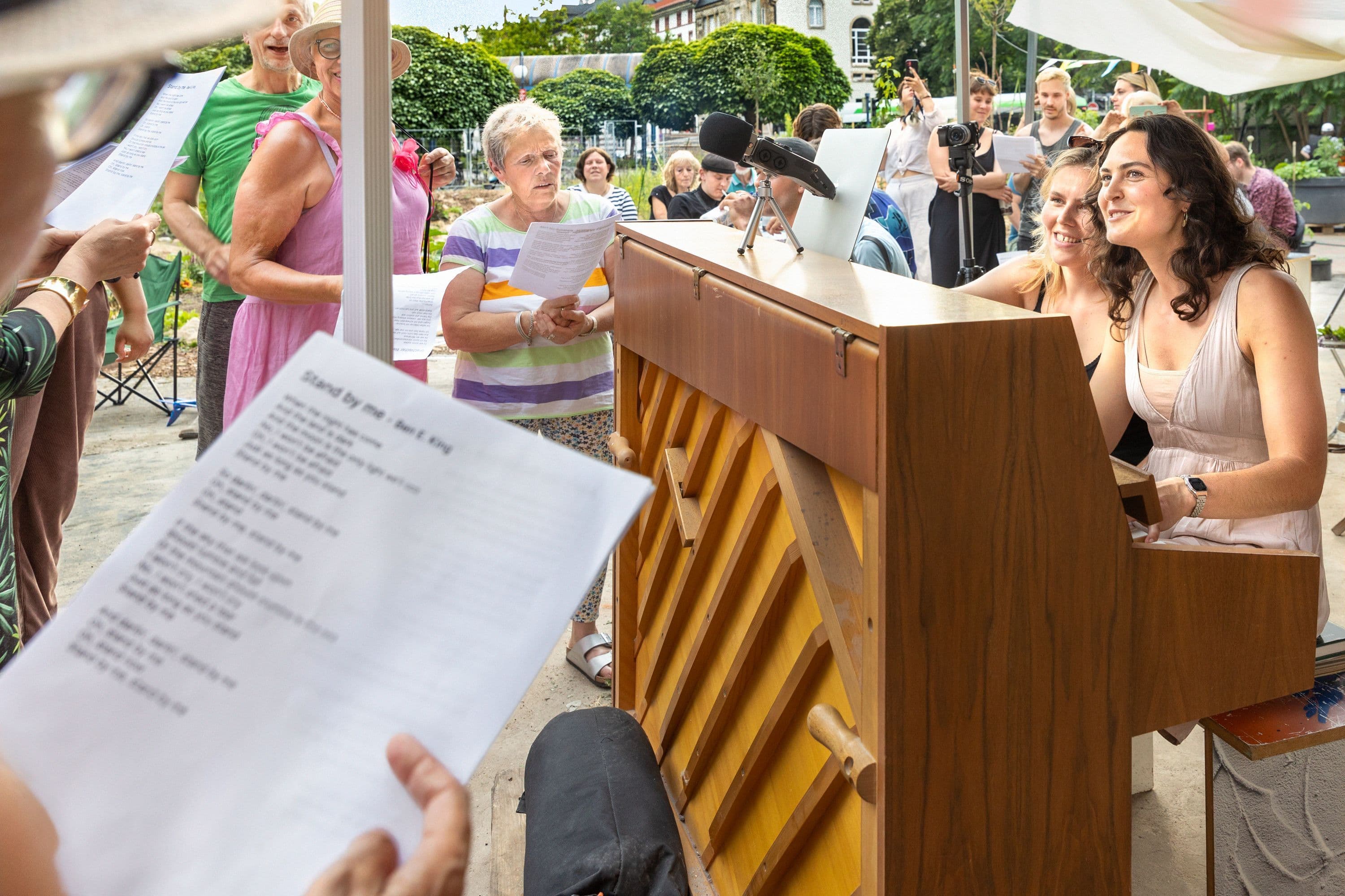 Ein Gruppe Menschen, die gemeinsam neben einem Klavier singen
