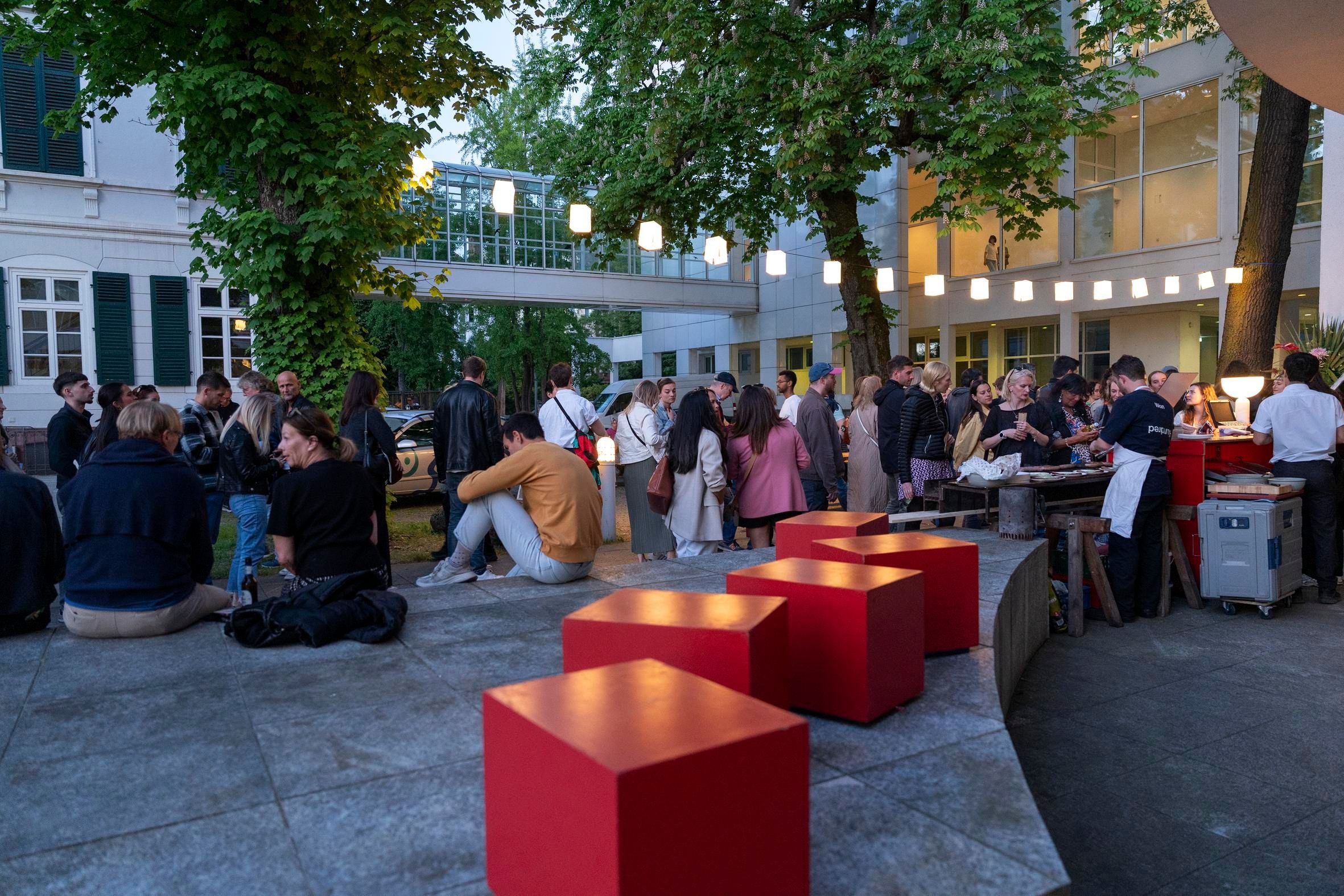 Personen sitzen beim Museum Angewandte Kunst zusammen unter Lampions und Bäumen.